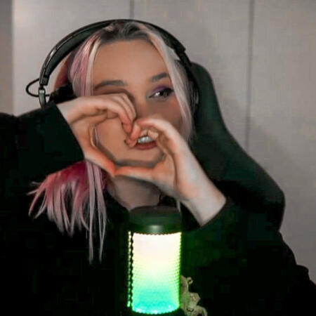 the image depicts nihachu, a white woman with dyed pink hair. she holds her hands up to form a heart.